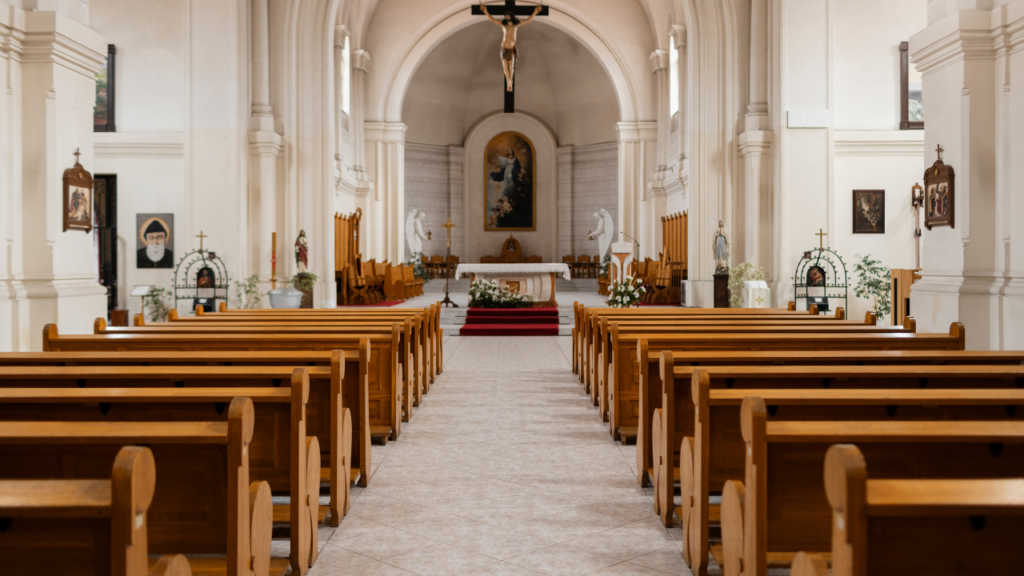 Interior de uma igreja católica com bancos de madeira, um altar central e um crucifixo acima.