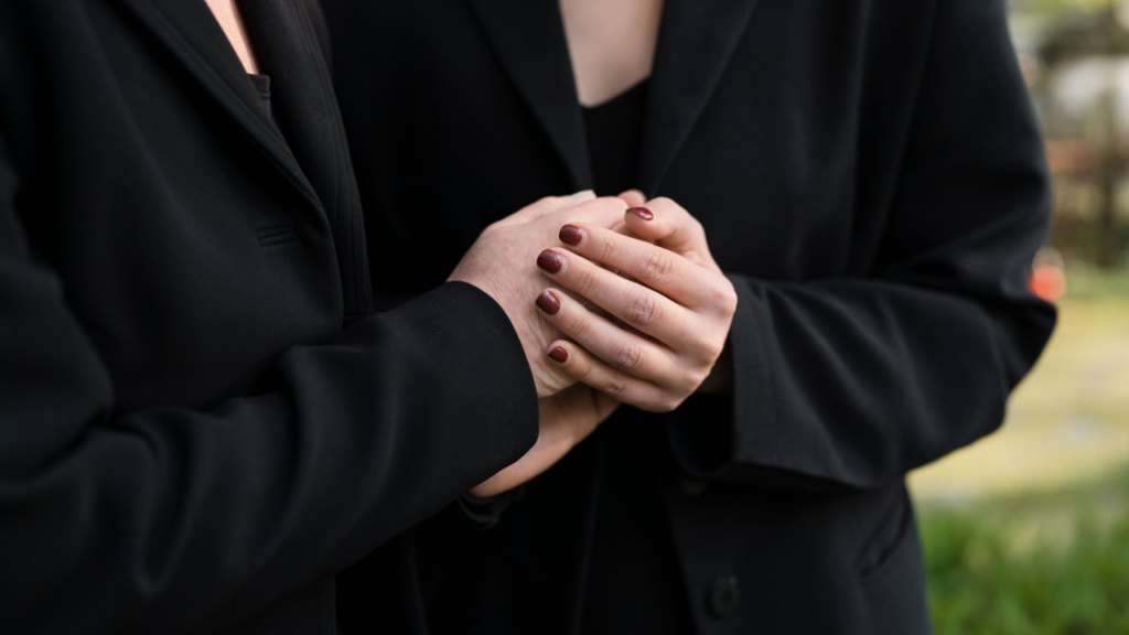 Duas pessoas vestidas de preto segurando as mãos em um gesto de conforto ou apoio.